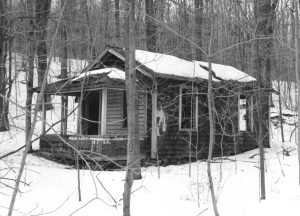 A run-down small bungalow in winter, with snow on the roof and ground.